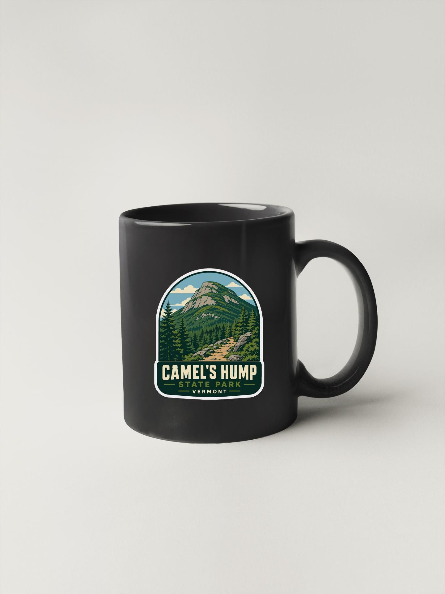 A black coffee mug with a graphic design depicting a mountain landscape and the text "CAMEL'S HUMP" printed on it.