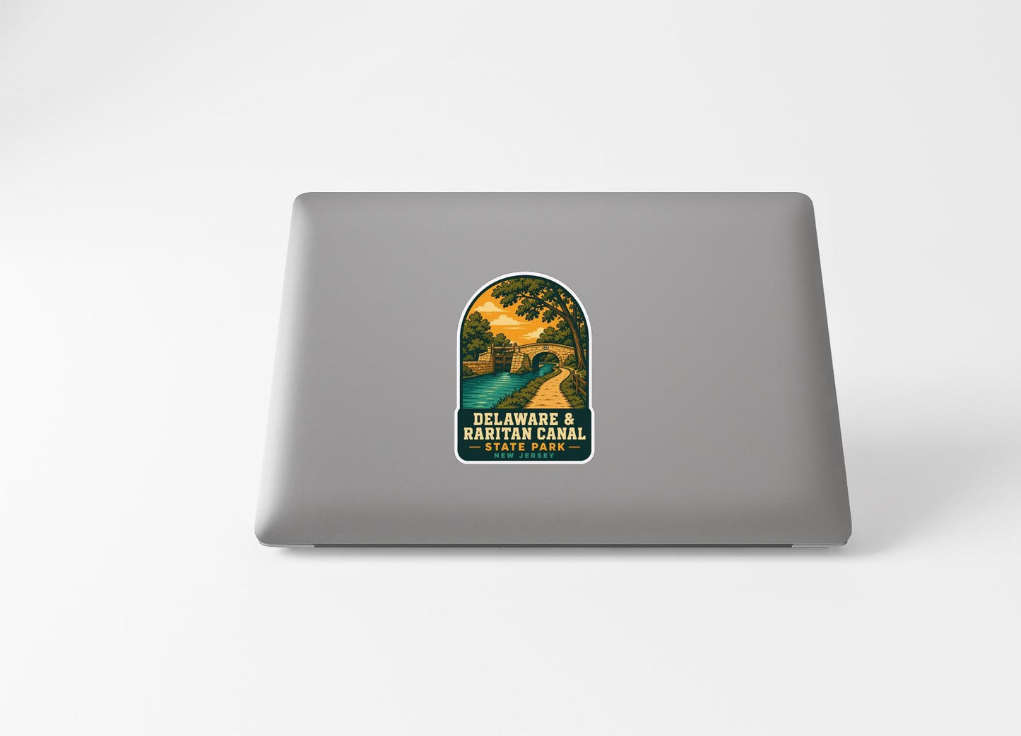 A sticker on the back of a laptop, depicting a scenic landscape with a bridge and trees.