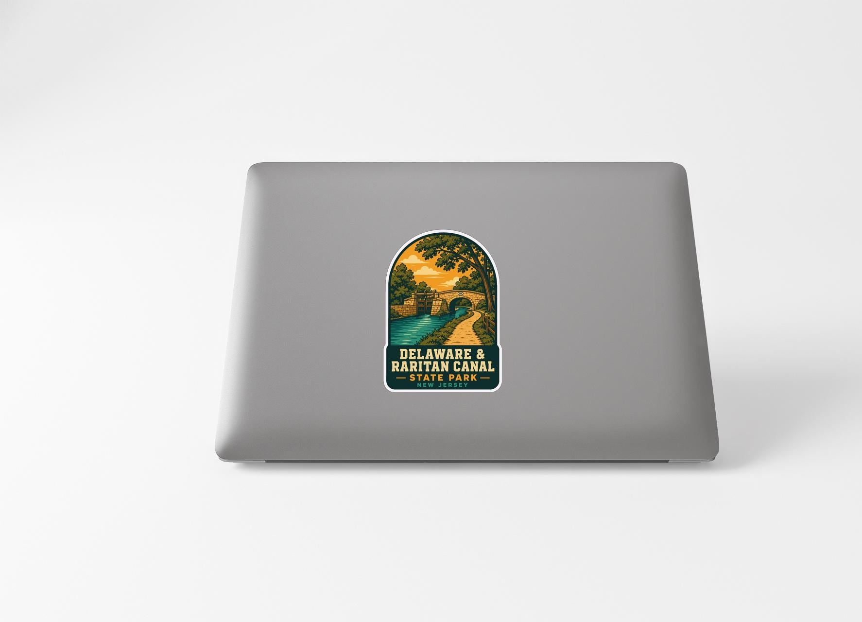 A sticker on the back of a laptop, depicting a scenic landscape with a bridge and trees.
