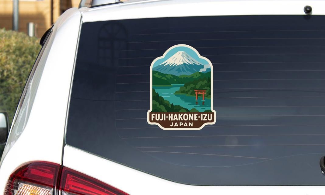 A sticker on the rear window of a car, depicting a scenic landscape with a mountain and a river, along with the text "FUJI-HAKONE-IZU JAPAN".