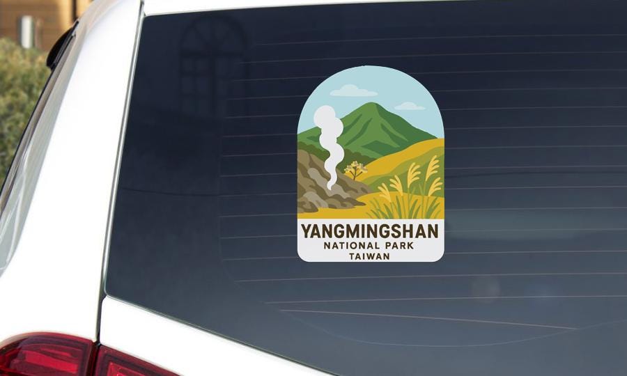 A sticker on the rear window of a car, depicting a scenic landscape with mountains, grass, and a winding road.