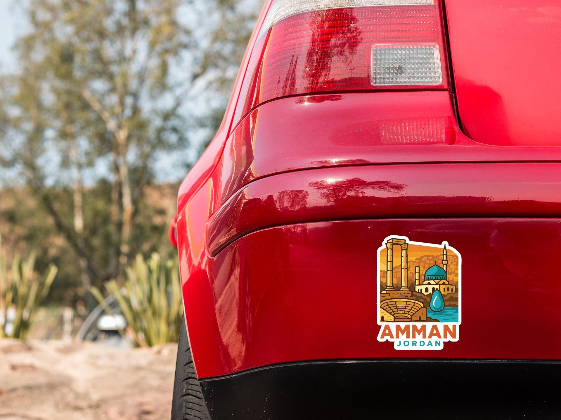the rear end of a red car with a sticker on the back window that features an illustration of a cityscape with a mosque and a river.