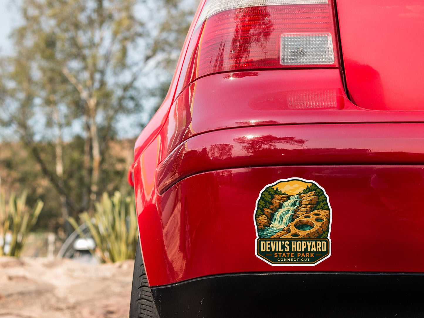 the rear end of a red car with a sticker on the trunk that says "Devil's Hypyard State Park Connecticut".