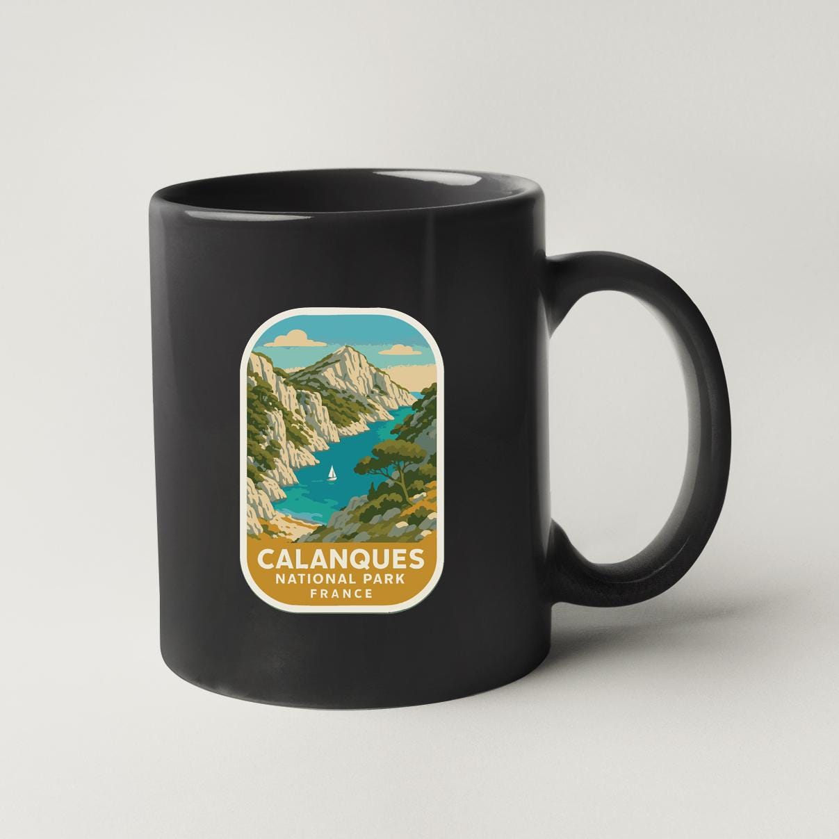 A black coffee mug with a label that features an illustration of a scenic landscape with mountains, a river, and a sailboat.