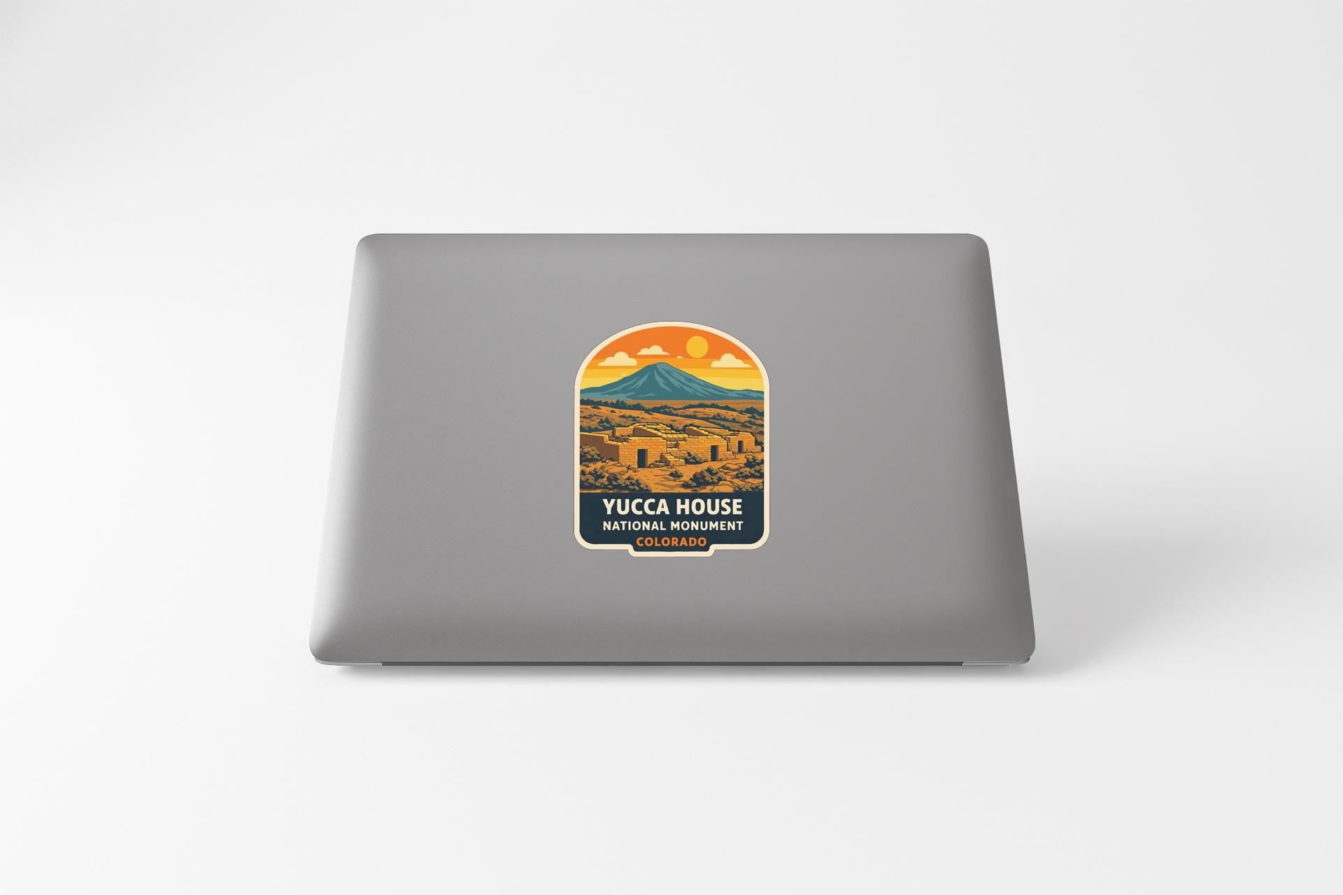 A sticker on the back of a laptop, depicting a mountain landscape with a sunset in the background.