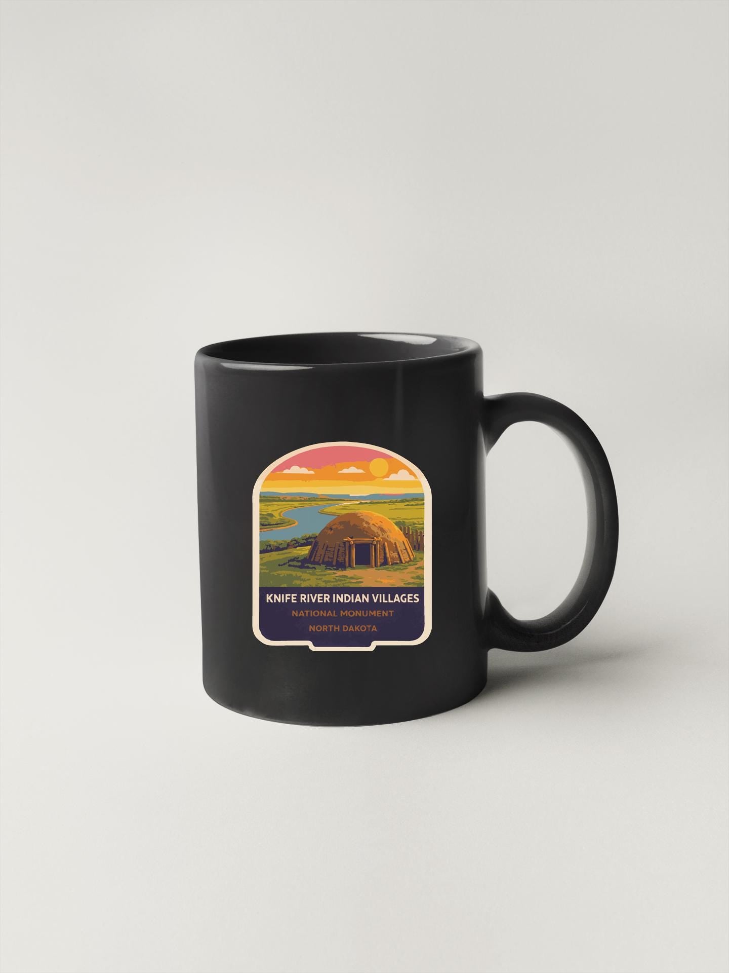 A black coffee mug with a label depicting a Native American village, specifically Knifes River Indian villages, located in North Dakota.