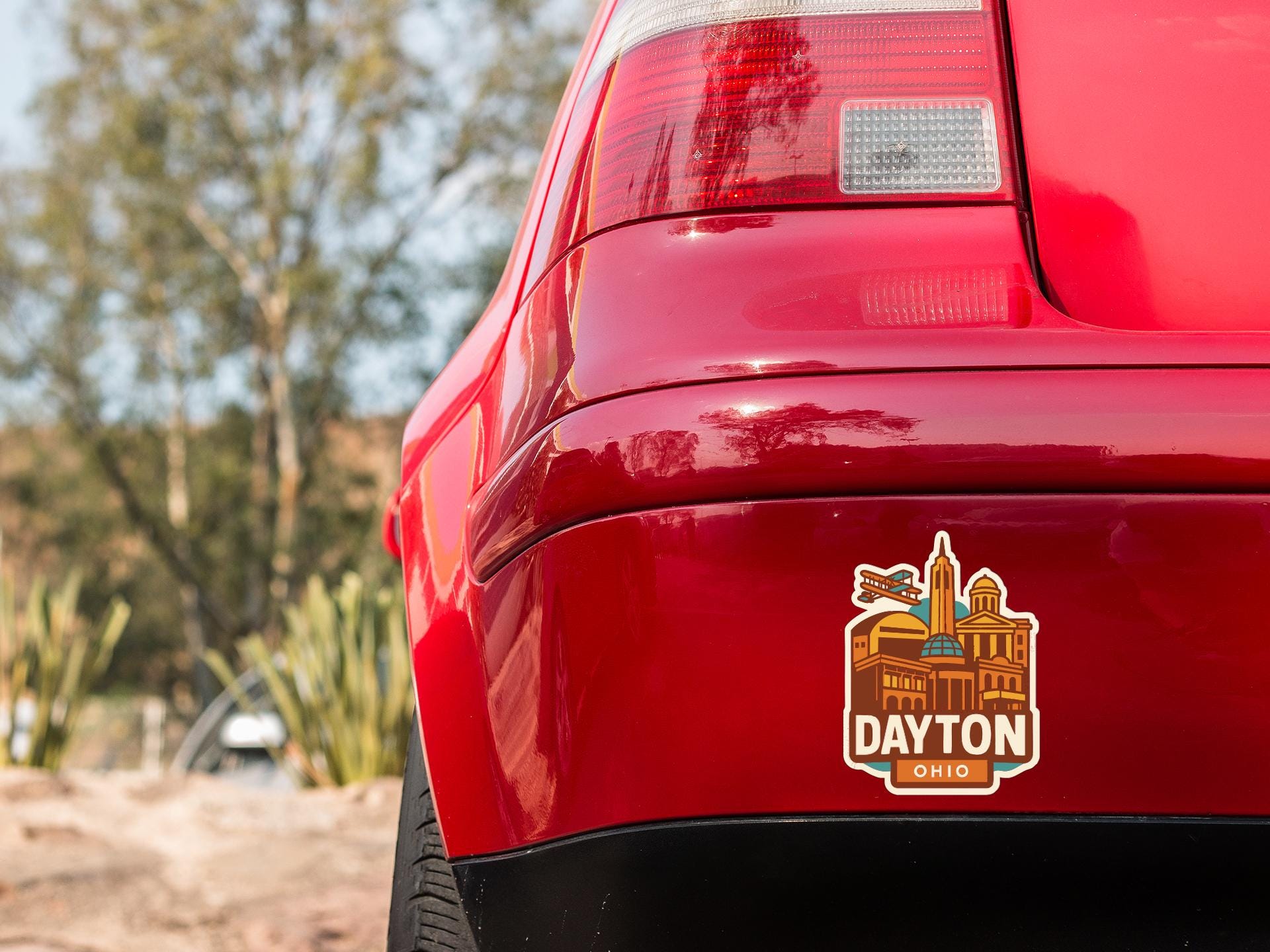 the rear end of a red car with a sticker on the trunk that says "DAYTON OHIO".