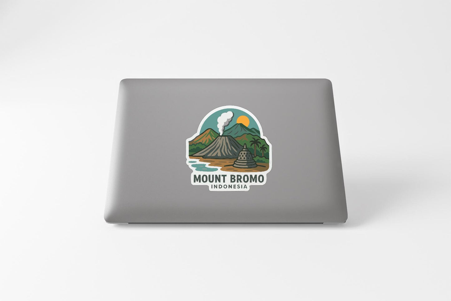 a sticker on the back of a laptop that depicts a mountain landscape with a volcano, a palm tree, and a body of water.