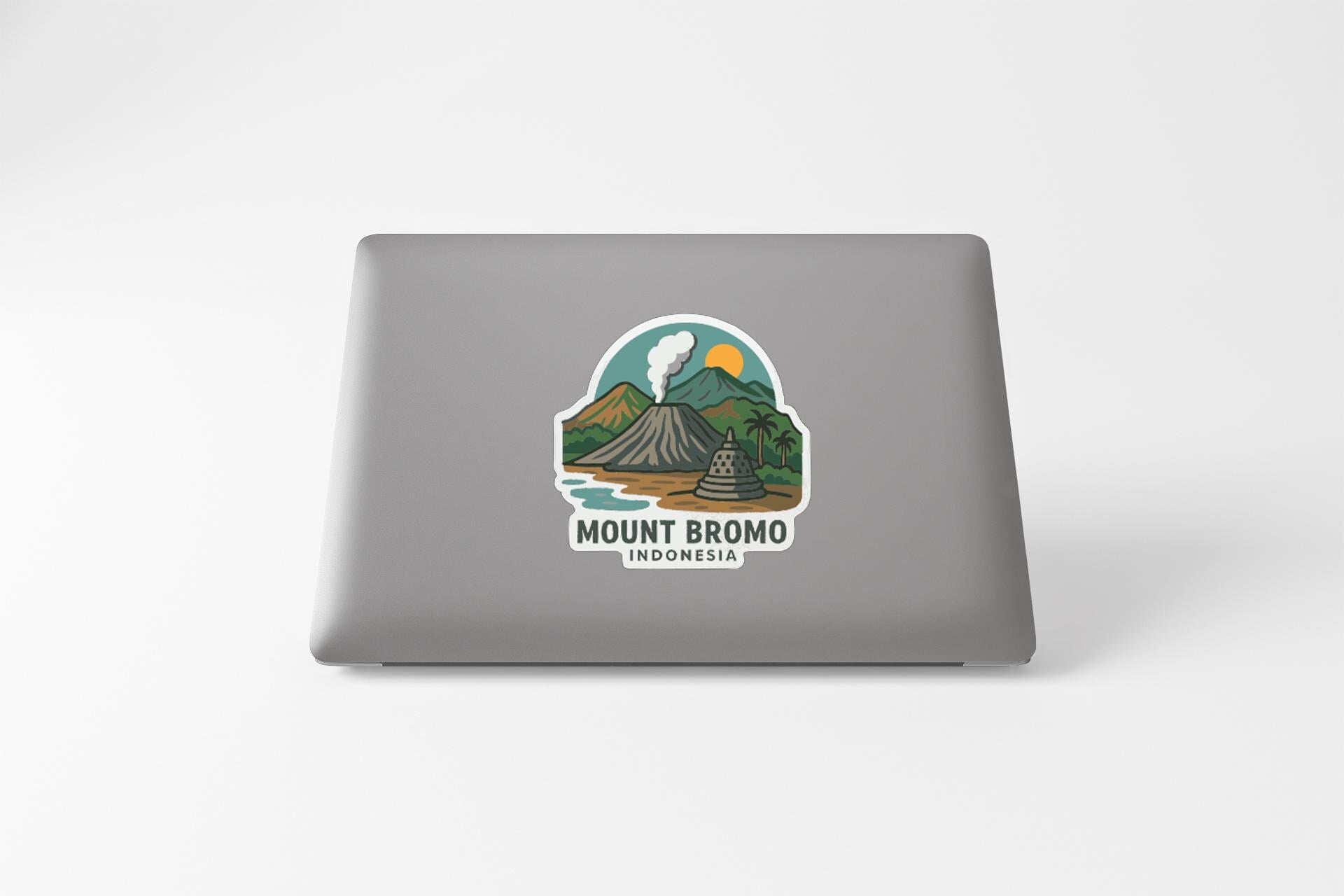 a sticker on the back of a laptop that depicts a mountain landscape with a volcano, a palm tree, and a body of water.