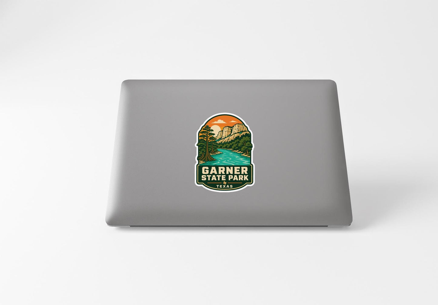 A sticker on the back of a laptop, depicting a scenic landscape with mountains, a river, and a sunset.