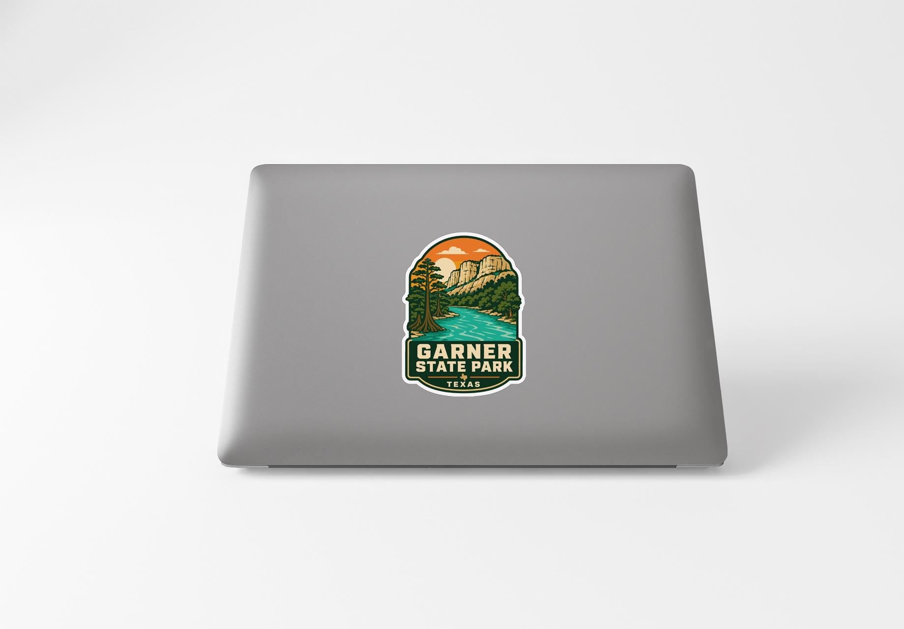 A sticker on the back of a laptop, depicting a scenic landscape with mountains, a river, and a sunset.