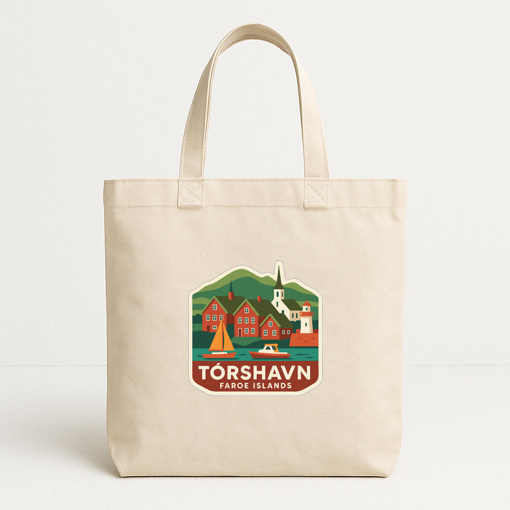 A beige tote bag with a graphic design depicting a scenic town or village, featuring buildings, a church, and a sailboat.