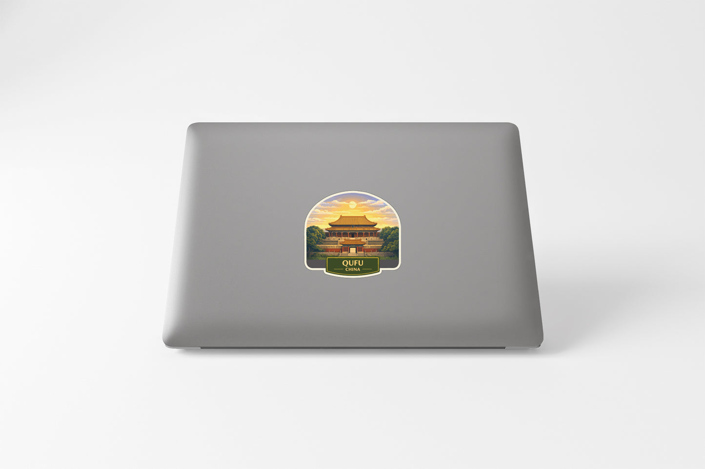 A sticker depicting a temple with a sunset in the background is placed on the back of a laptop.