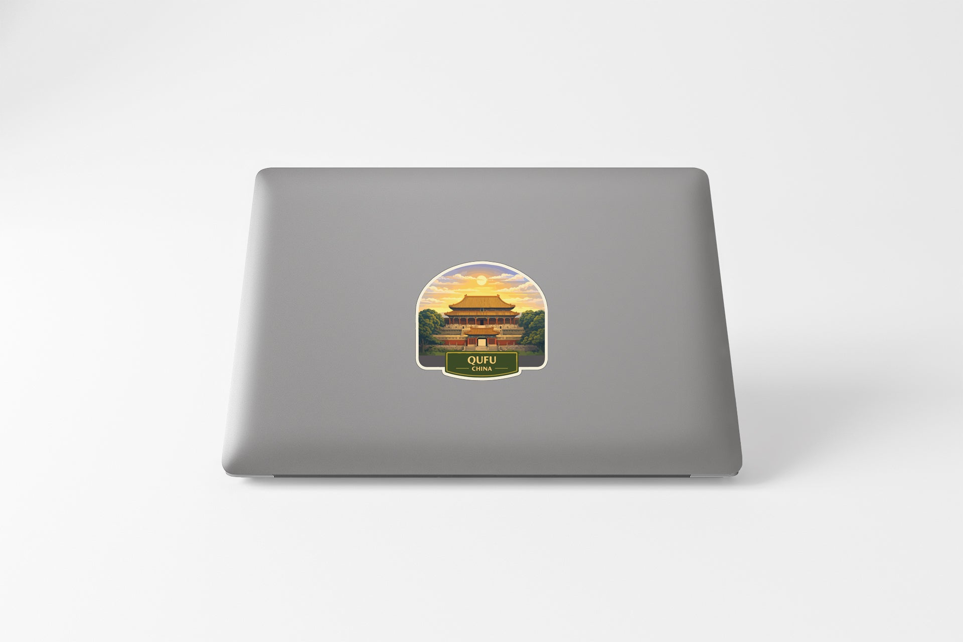 A sticker depicting a temple with a sunset in the background is placed on the back of a laptop.