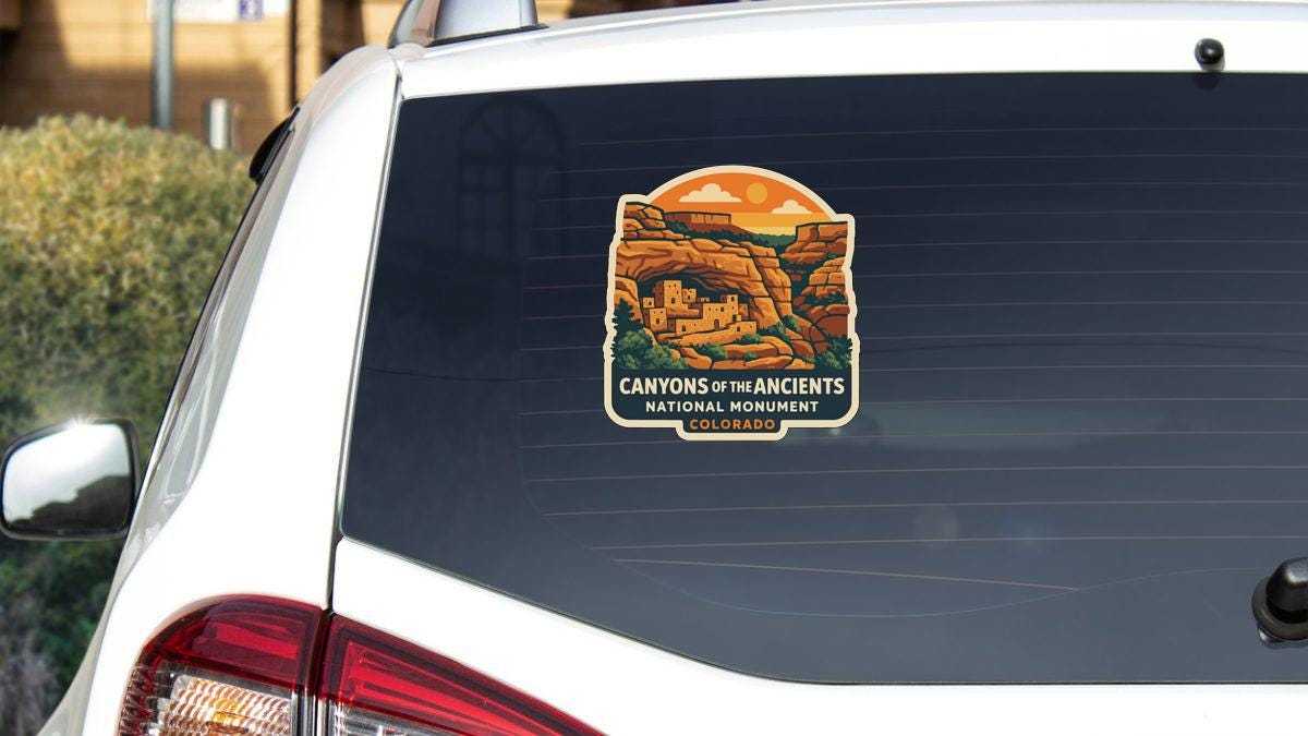 A sticker on the rear window of a white car, depicting a scenic landscape with mountains and a town.