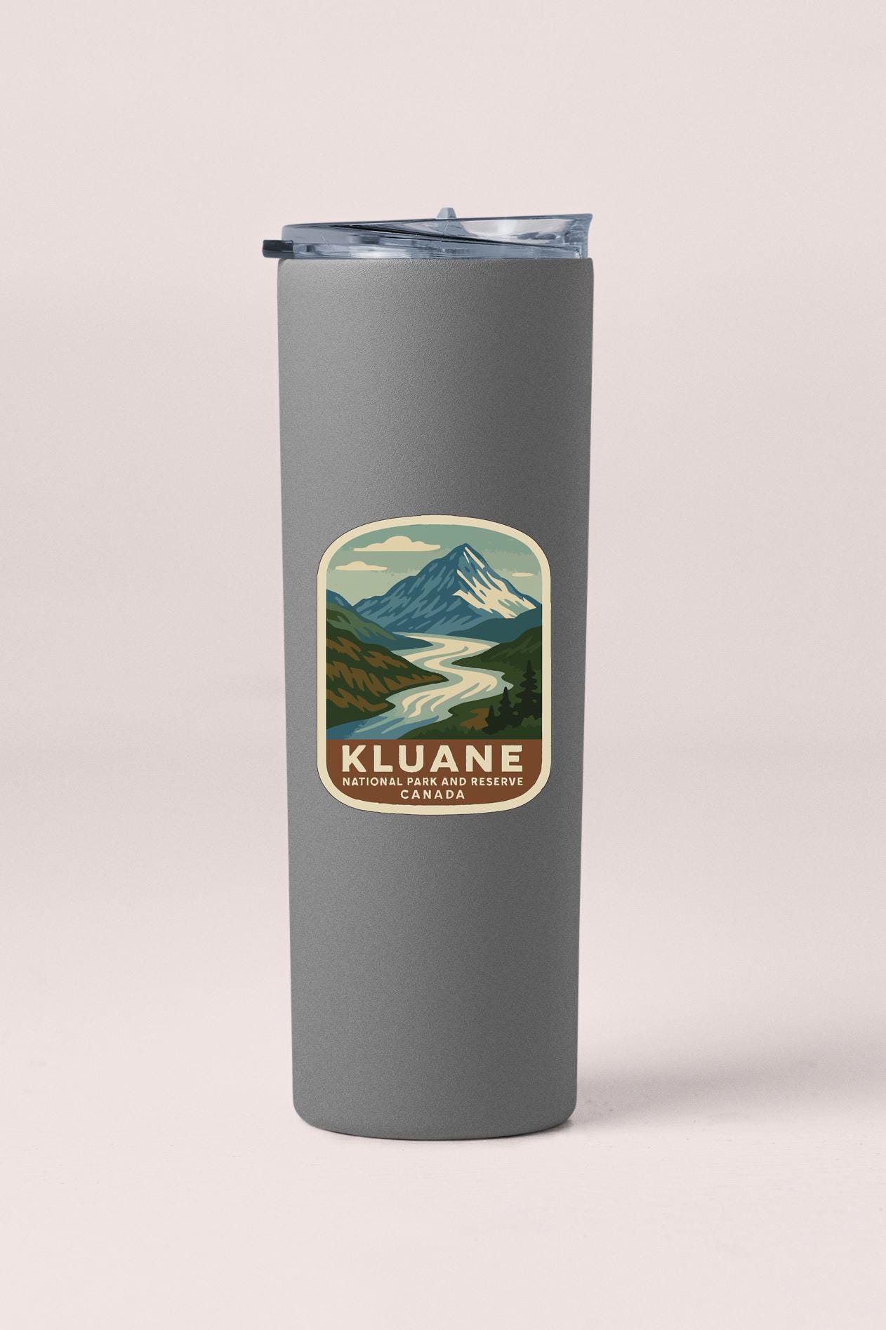 A gray insulated tumbler with a sticker depicting a mountain landscape and the text "Kluane National Park and Preserve, Canada".