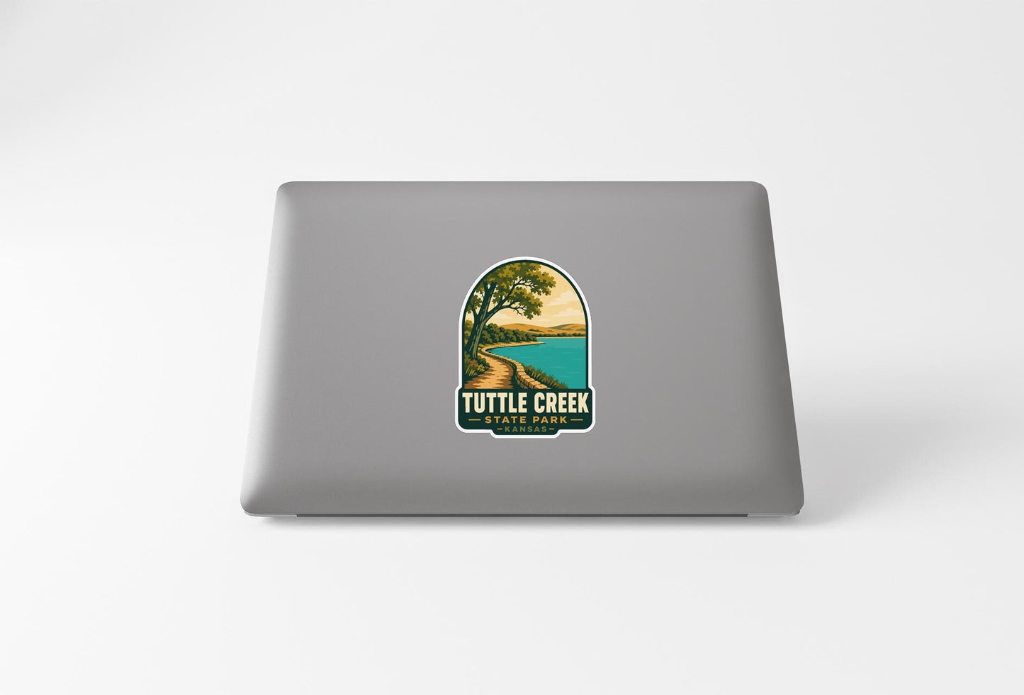 A sticker on the back of a laptop, depicting a scenic landscape with a lake and a tree.