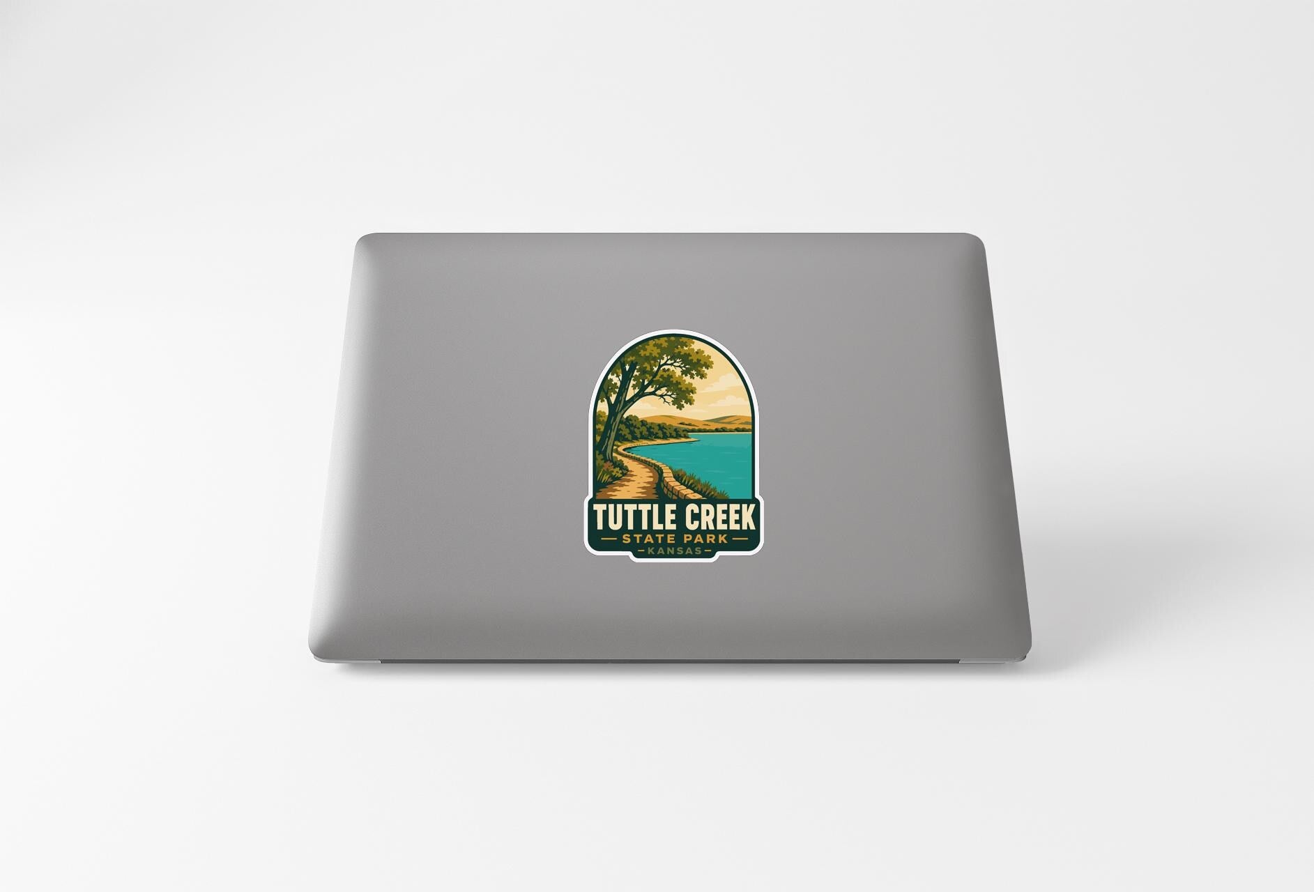 A sticker on the back of a laptop, depicting a scenic landscape with a lake and a tree.