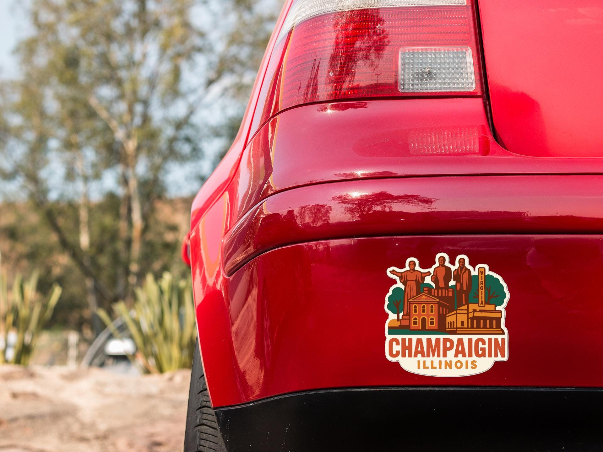 the rear end of a red car with a sticker on the trunk that says "CHAMPAIGN, ILLINOIS".