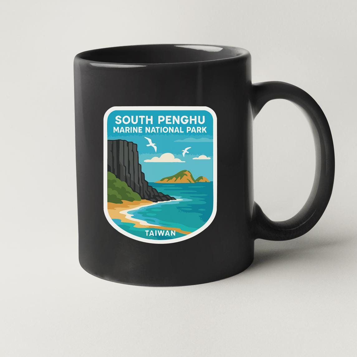 A black coffee mug with a sticker depicting a scenic coastal landscape, including a cliff, beach, and ocean.