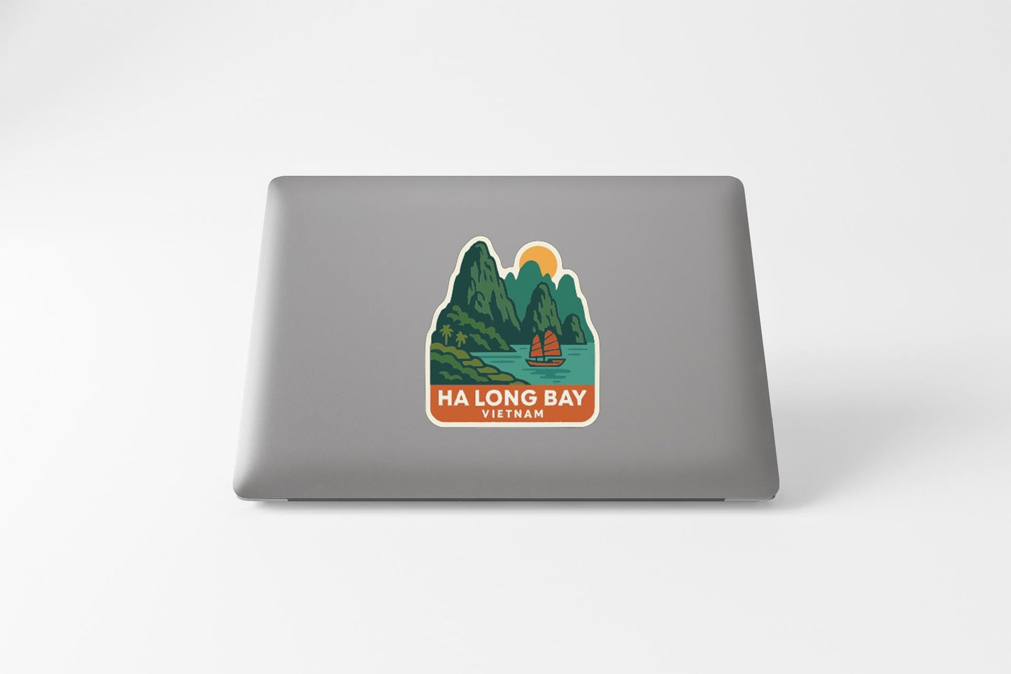 a sticker or decal on the back of a laptop, depicting a scenic landscape with mountains, a river, and a boat.