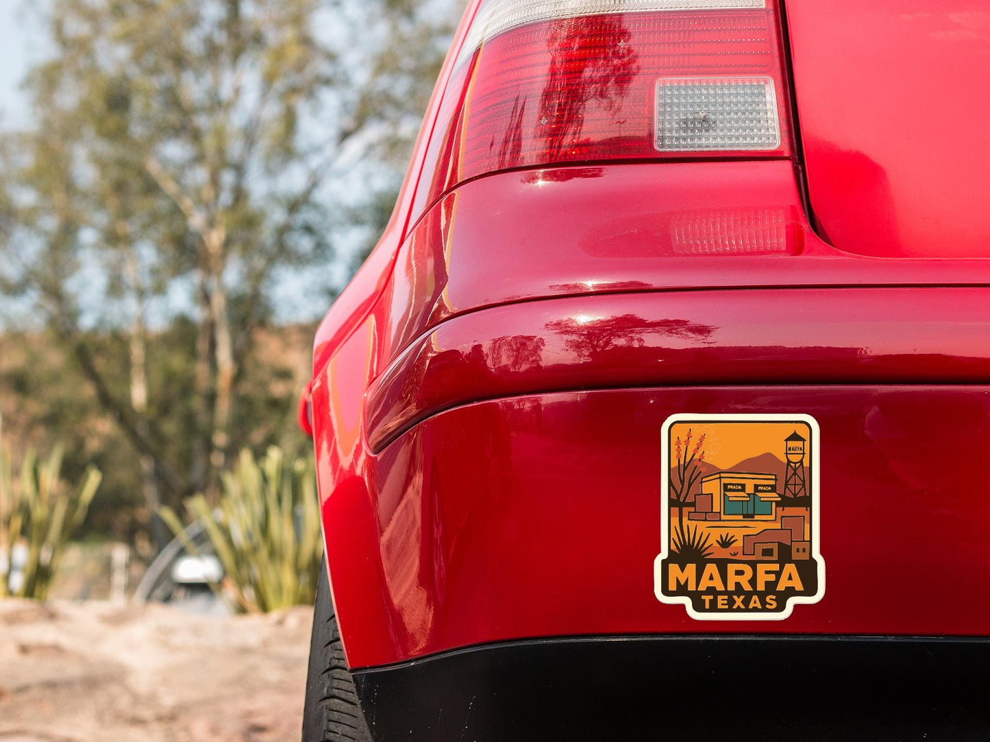 the rear end of a red car with a Marfa, Texas license plate sticker on the trunk.