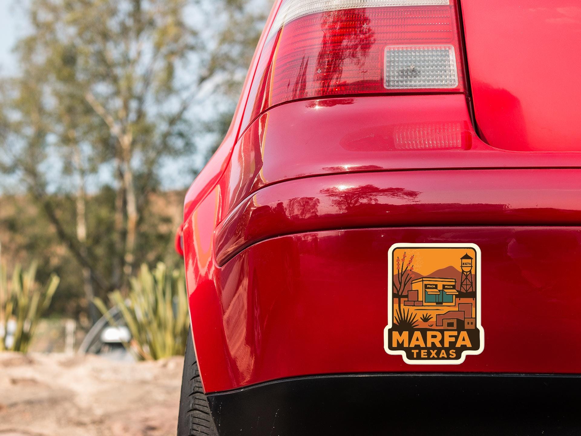 the rear end of a red car with a Marfa, Texas license plate sticker on the trunk.