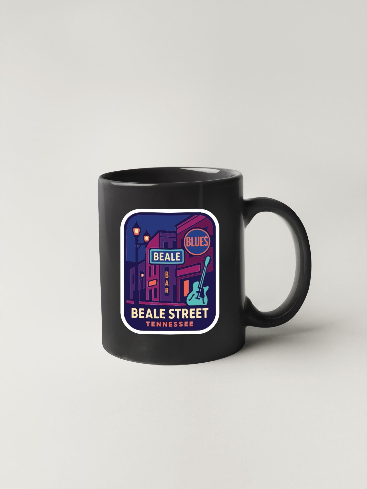 A black coffee mug with a colorful graphic design depicting a street scene, including a blues bar and the text "Beale Street, Nashville".