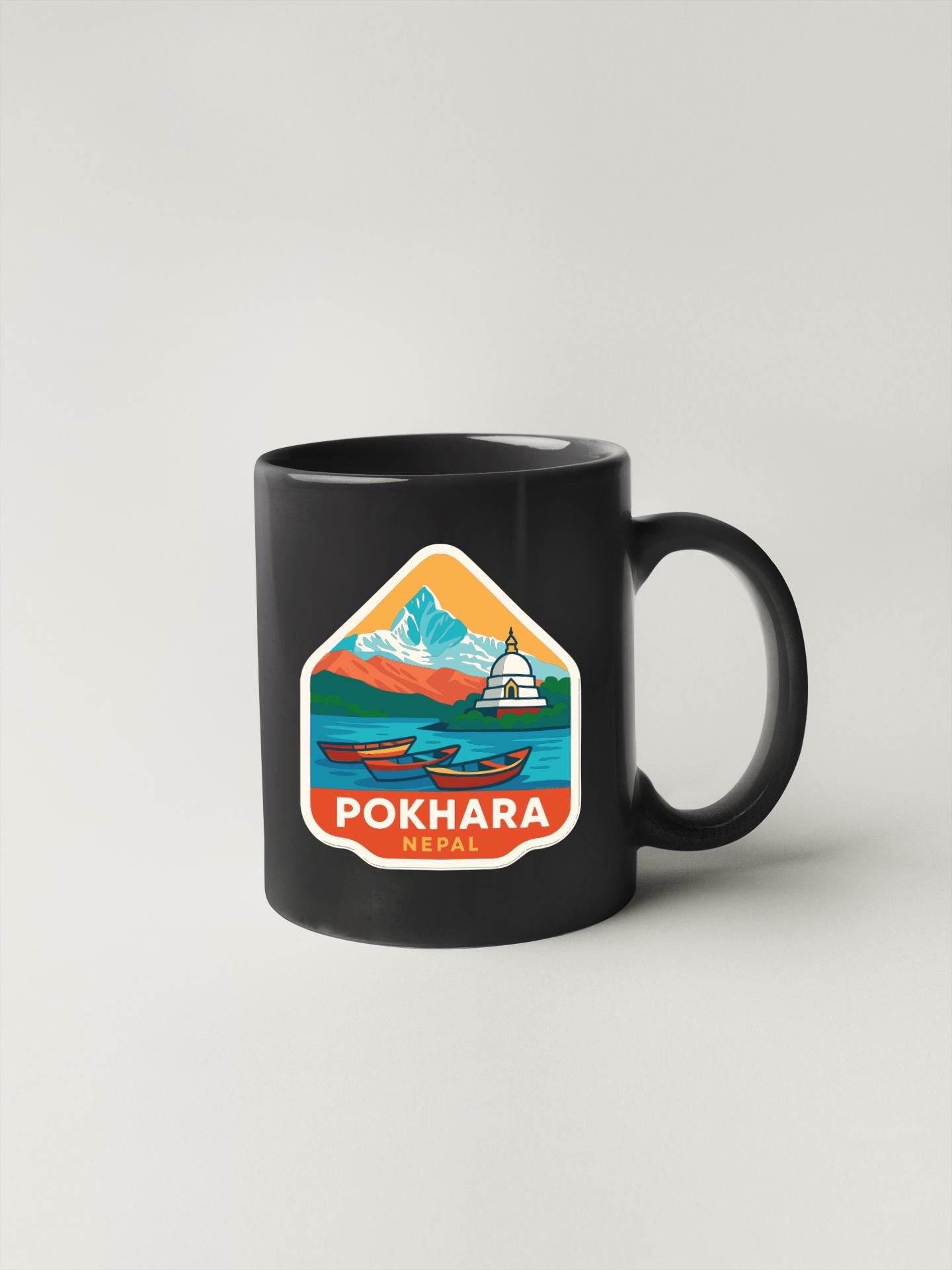 A black coffee mug with a colorful sticker depicting a mountain landscape and a temple.
