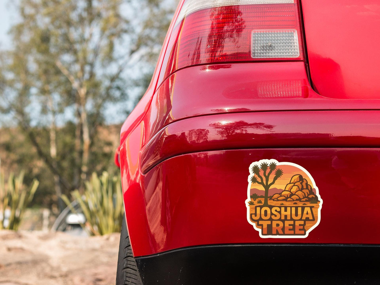 the rear end of a red car with a sticker on the trunk that says " Joshua Tree".