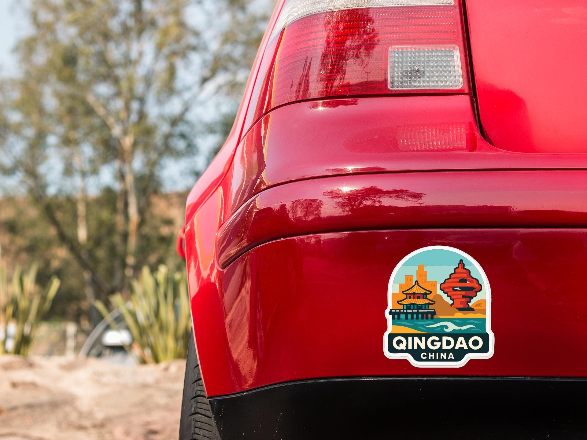 the rear end of a red car with a sticker on the trunk that says "Qingdao China".