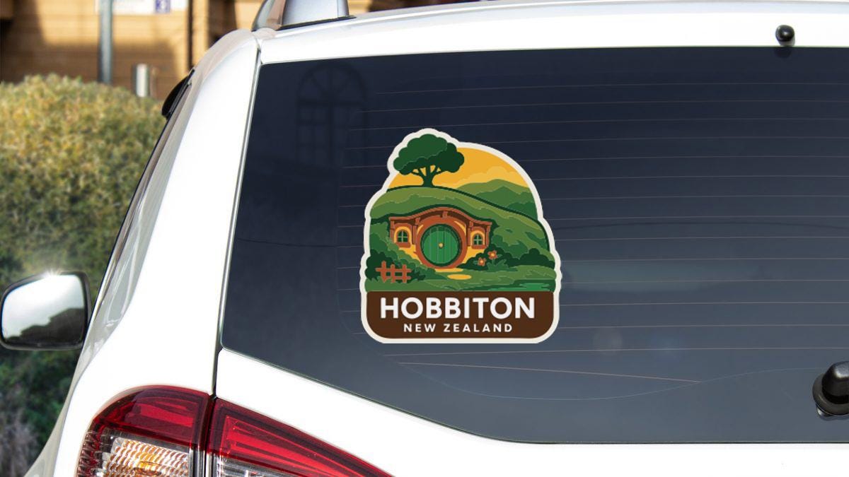 A sticker on the rear window of a car that features a depiction of a house with a tree and a castle, along with the text "HOBBITON NEW ZEALAND".