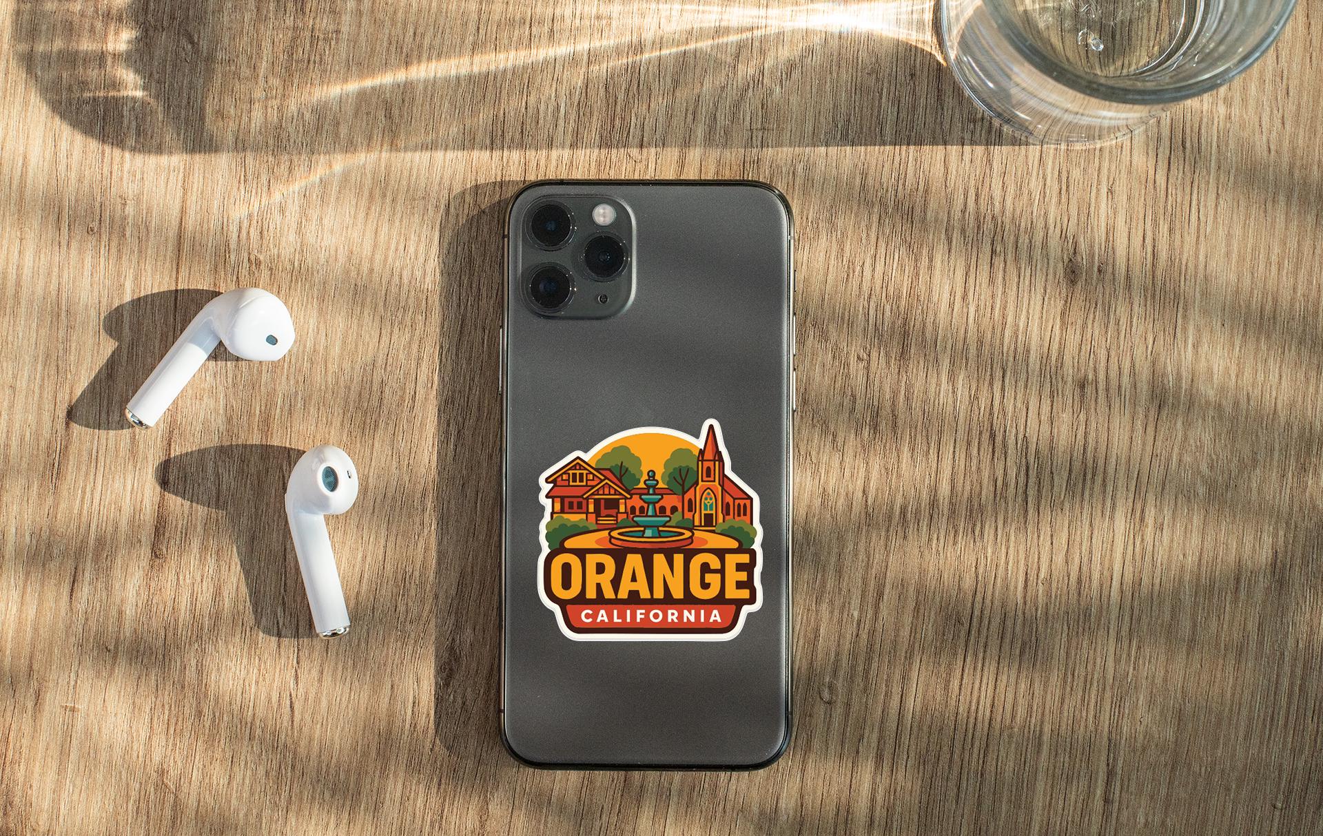 a smartphone with a sticker of Orange California on it, placed on a wooden surface alongside a pair of white earbuds and a glass of water.