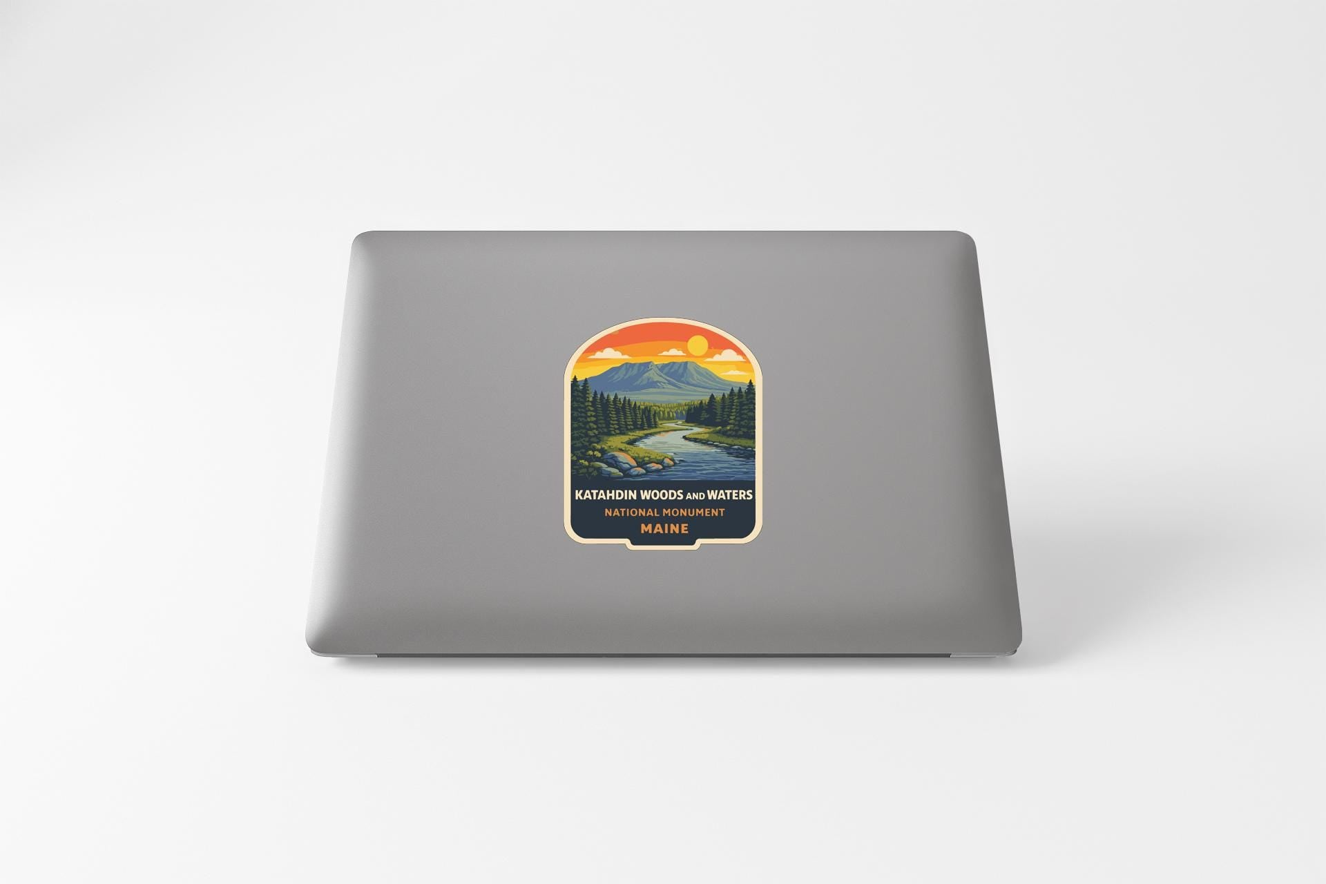 A sticker on the back of a laptop, depicting a scenic landscape with mountains, trees, and a river.