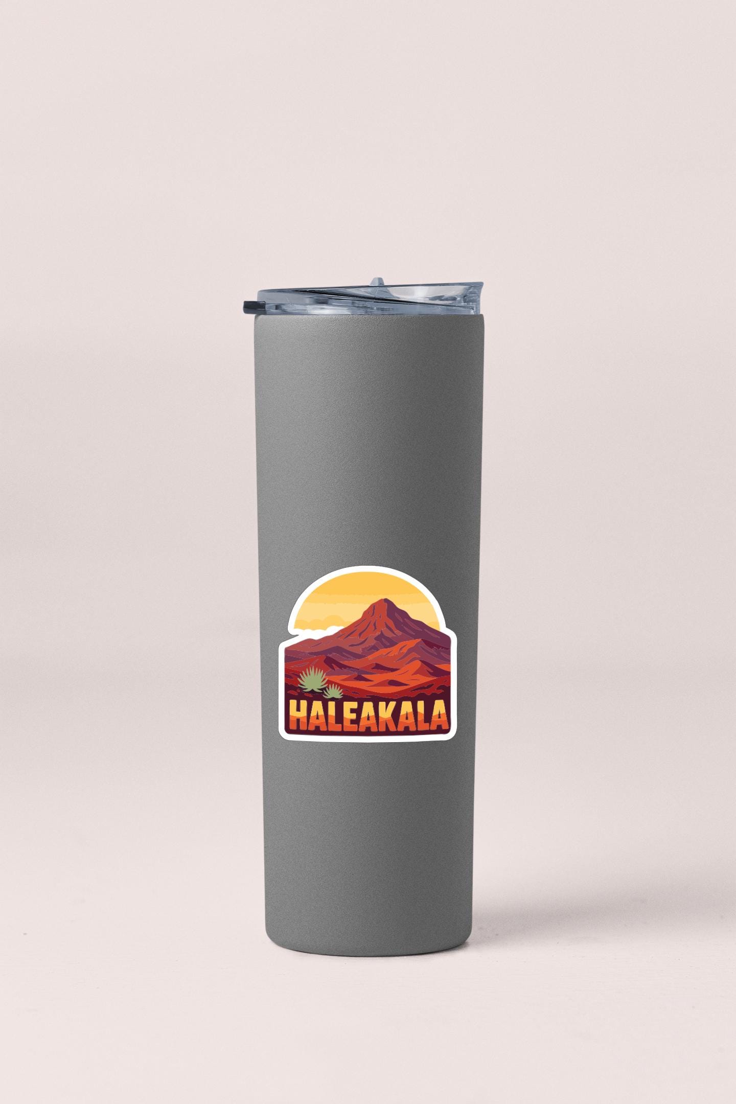 A gray insulated tumbler with a sticker depicting a mountain and the word "Haleakala" printed on it.