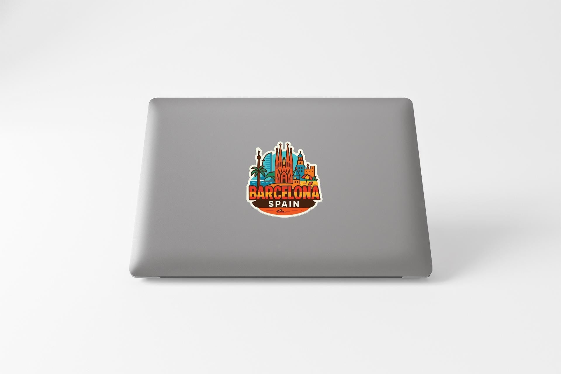 a sticker with a graphic of a city skyline and the text "BARCELONA SPAIN" on a grey laptop.