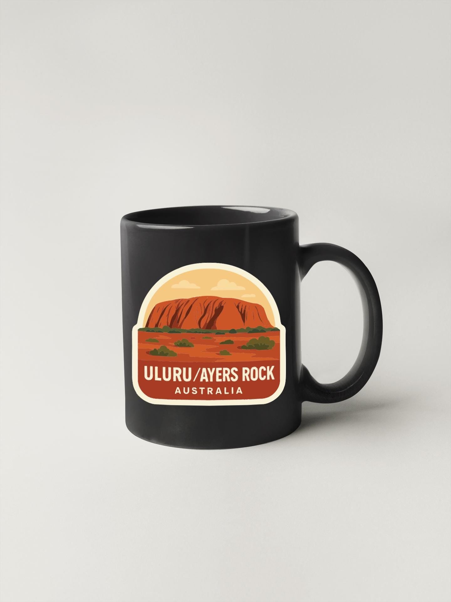 A black coffee mug with a graphic design depicting Uluru, a famous rock formation in Australia.