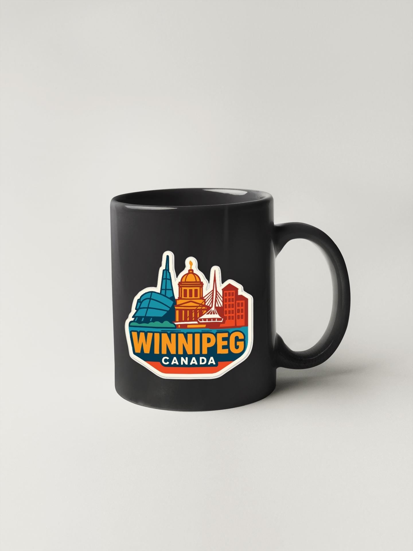 A black coffee mug with a colorful graphic of the downtown area of Winnipeg, Canada, featuring various landmarks and buildings.