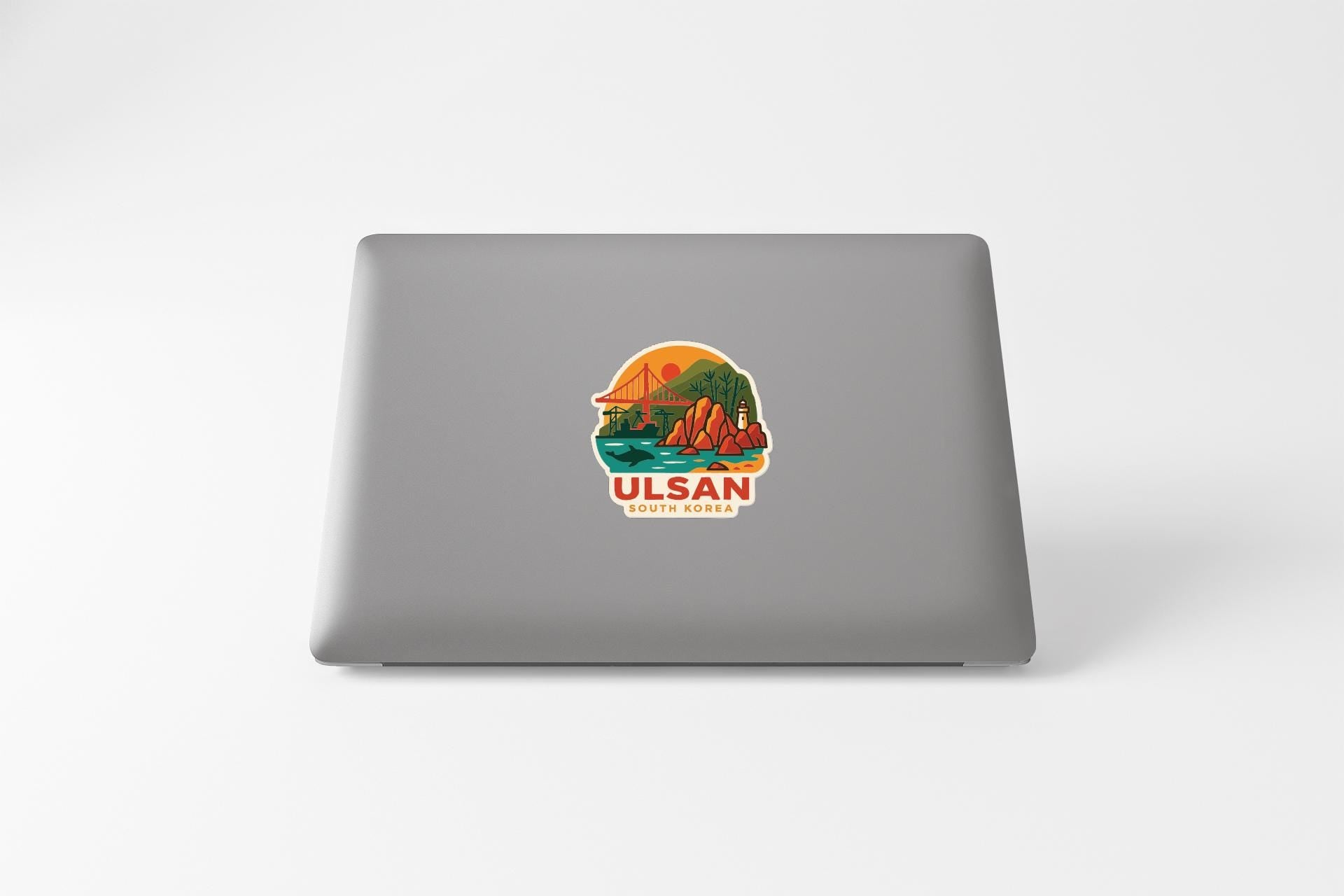 A sticker on the back of a laptop, depicting a scenic landscape with mountains, water, and a sunset.