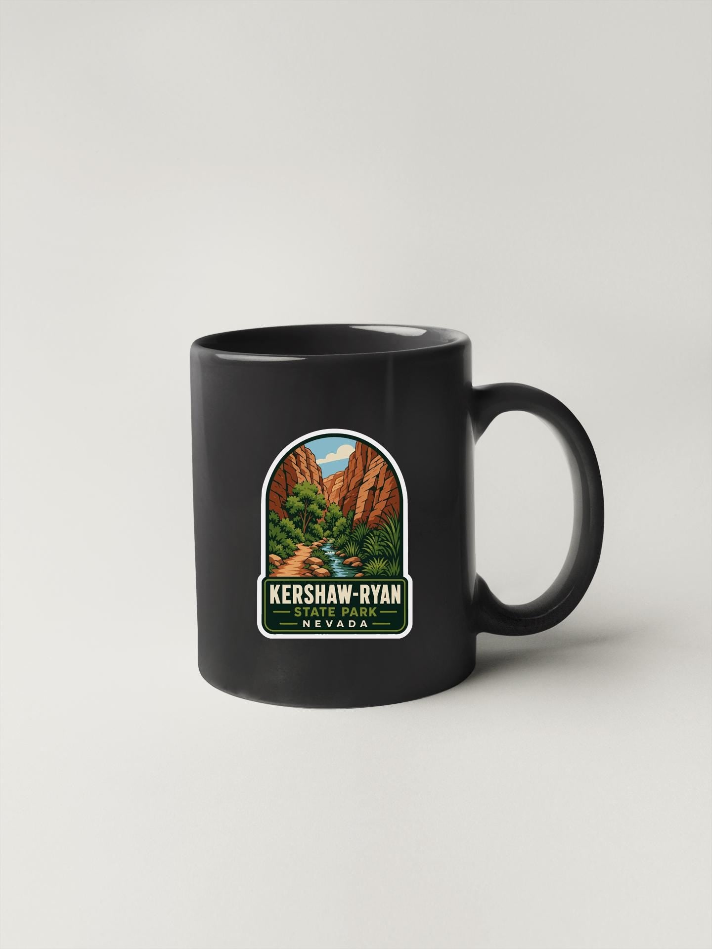 A black coffee mug with a sticker depicting a scenic landscape, including mountains and a river, along with the text "KERSHAW-RYAN NEVADA".