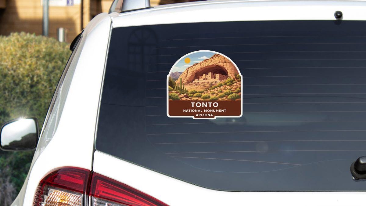 A sticker on the rear window of a white car, depicting the Tonto National Monument in Arizona.
