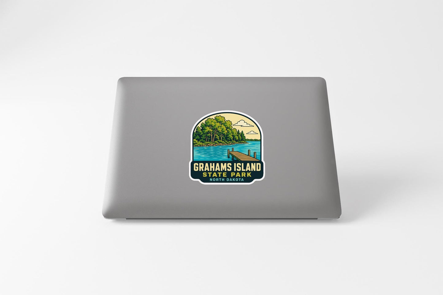 A sticker on the back of a laptop, depicting a scenic landscape with a lake, trees, and a dock.
