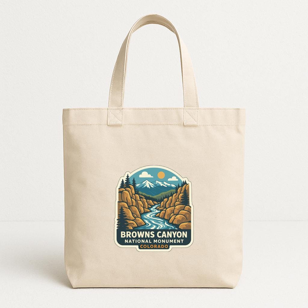 A beige tote bag with a printed design depicting a scenic landscape featuring a river, mountains, and a sun.