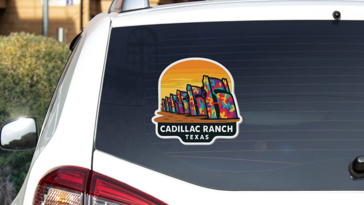 A sticker on the rear window of a white vehicle, depicting a colorful illustration of a desert landscape with buildings in the background.