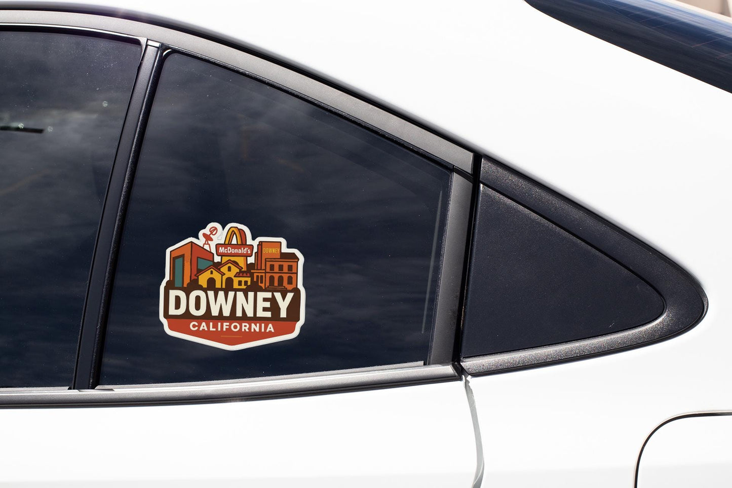A sticker on the side of a car window, featuring a cityscape and the text "DOWNEY, CALIFORNIA".