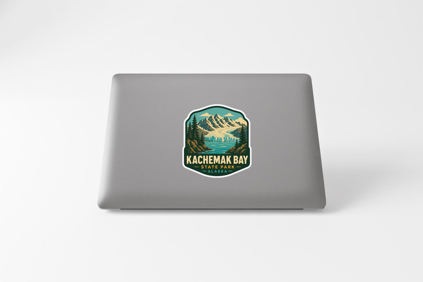 A sticker on the back of a laptop, depicting a scenic mountain landscape with a lake and pine trees.