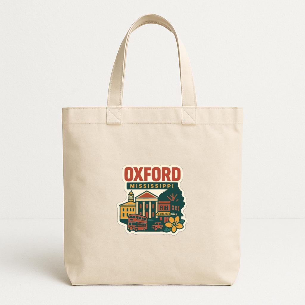 A beige tote bag with a printed design depicting a cityscape and the text "Oxford Mississippi" printed on it.