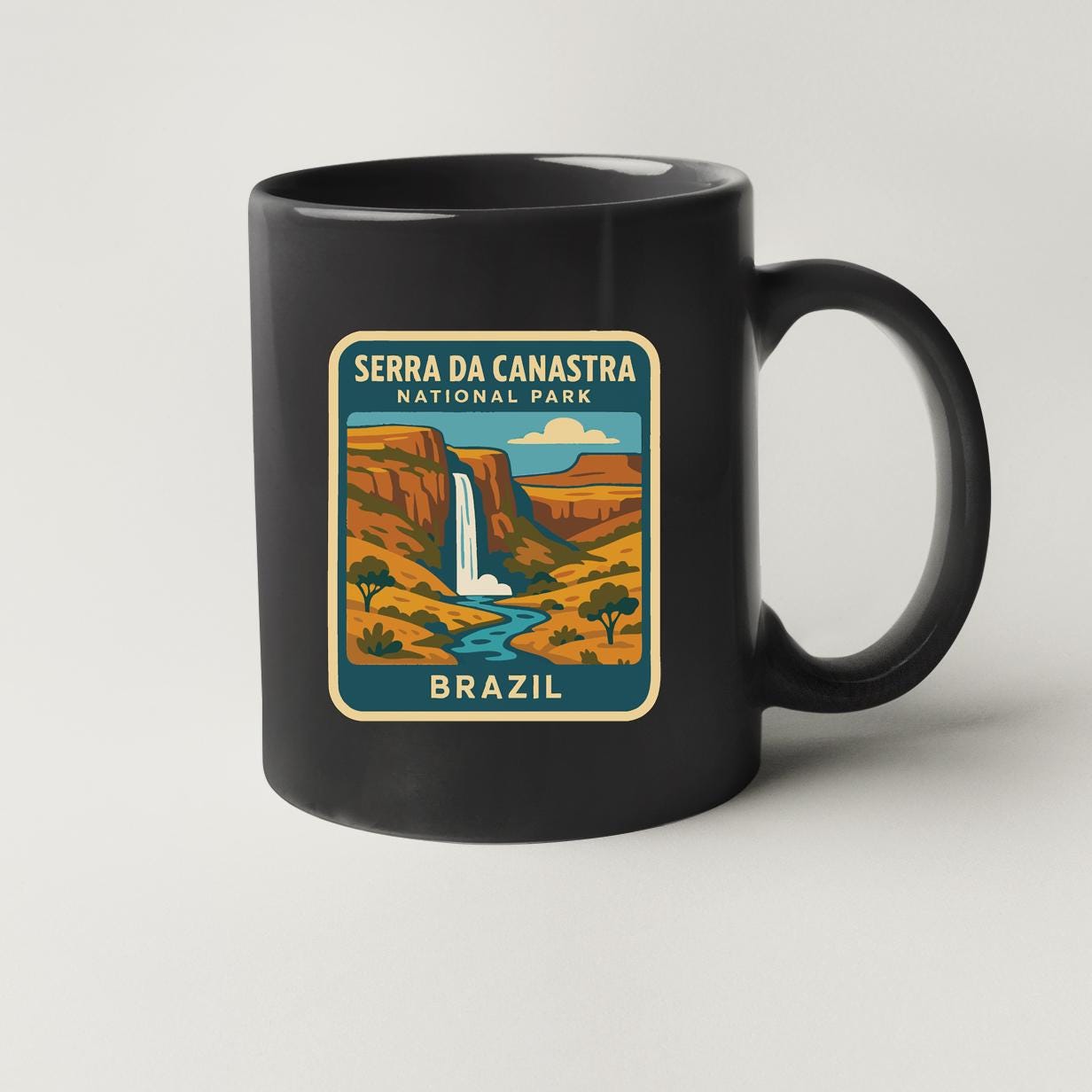 A black coffee mug with a colorful illustration of a waterfall and mountains, representing the Serra da Canastra National Park in Brazil.