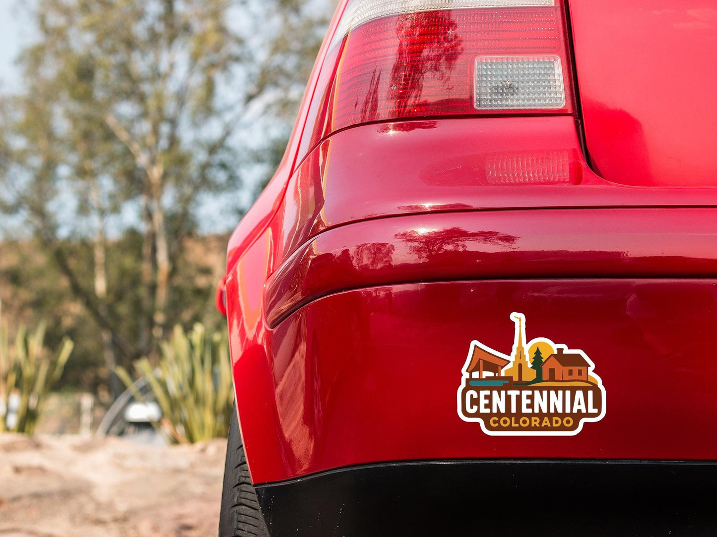 the rear end of a red car with a Centennial Colorado logo sticker on the trunk.