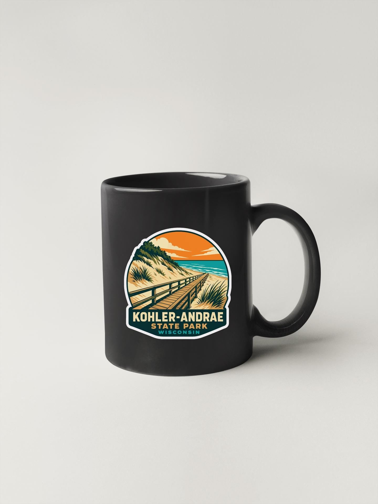 A black coffee mug with a graphic design depicting a beach scene and a path leading to a cliff.